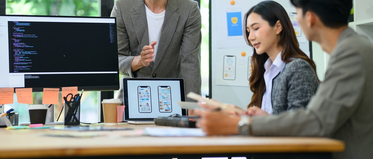 Young Asian developer presents mobile app UI UX wireframes and code to colleagues in a collaborative office brainstorm session, ideal for tech and startup concepts.